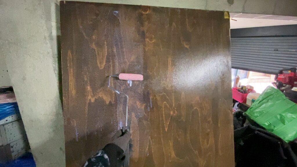 ローラーバケを使ってコンパネの表面にワックスを塗装している様子。