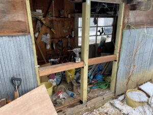 破損した物置内部に新たに組み込まれた木材と構造体。修理の初期段階。