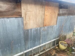 修理後の物置の外観。波板と補強された木製パネルが取り付けられた状態。