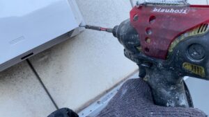 インパクトドライバーで新しい換気フードを外壁にビス打ちしている様子。