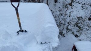 屋根の上からスコップを使って雪庇を切り落とす作業の様子。
