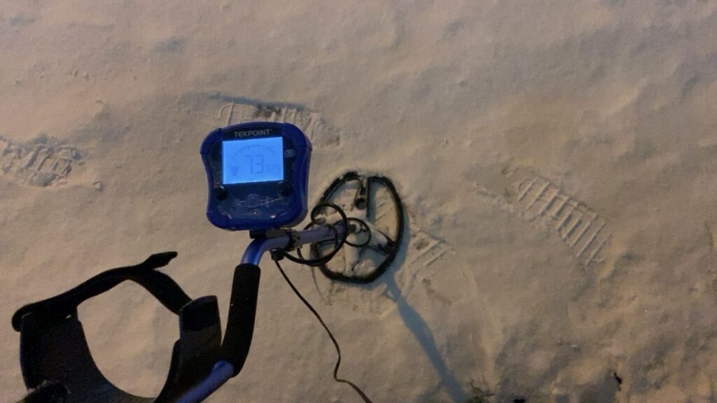 深夜の札幌市北区にて、金属探知機を使い雪の中を捜索する様子