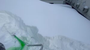 傾斜屋根の上で、雪を落とす場所を慎重に選定しながら作業する様子