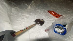 金属スコップを使い、スタックした車のお腹の下にある雪を書き出している様子