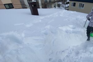 澄川の現場。スノーストッパールーフの上で雪下ろしを行うスタッフ