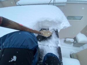 屋根の上から金属スコップを使い、雪庇を少しずつ削り落としている作業風景