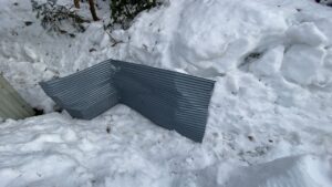 雪の中から掘り起こした折れ曲がった波トタン