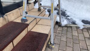 階段の段差に合わせて脚立の足を伸ばして設置している様子