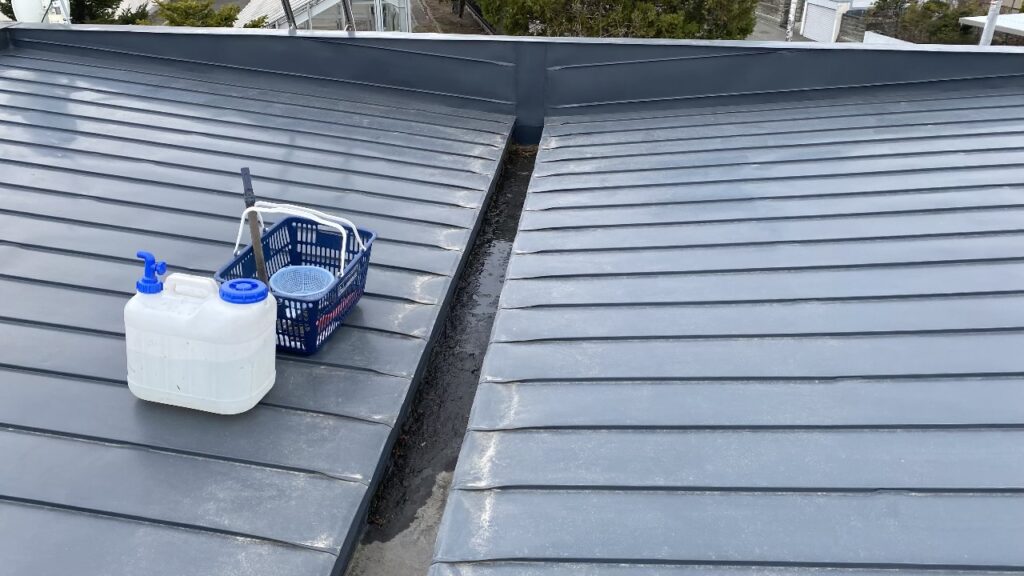 屋根に20リットルのタンクを運んで清掃作業を行う