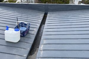 屋根に20リットルのタンクを運んで清掃作業を行う