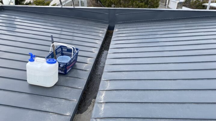 屋根に20リットルのタンクを運んで清掃作業を行う