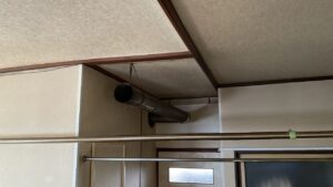 天井から針金で吊るされた長いステンレス煙突の様子
