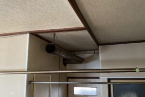 天井から針金で吊るされた長いステンレス煙突の様子