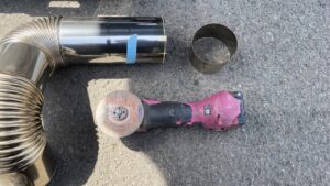 取り外したステンレス煙突を屋外でディスクグラインダーを使ってカットしている様子