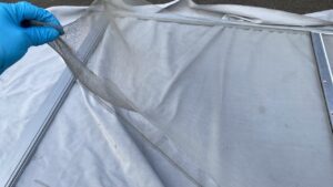 屋外に敷物を敷き、古い網戸から古い網を破り取り外している作業風景
