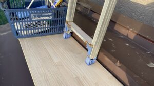 車庫の屋根の上に厚い木の板を敷き、その上にはしごの足を着地させている様子