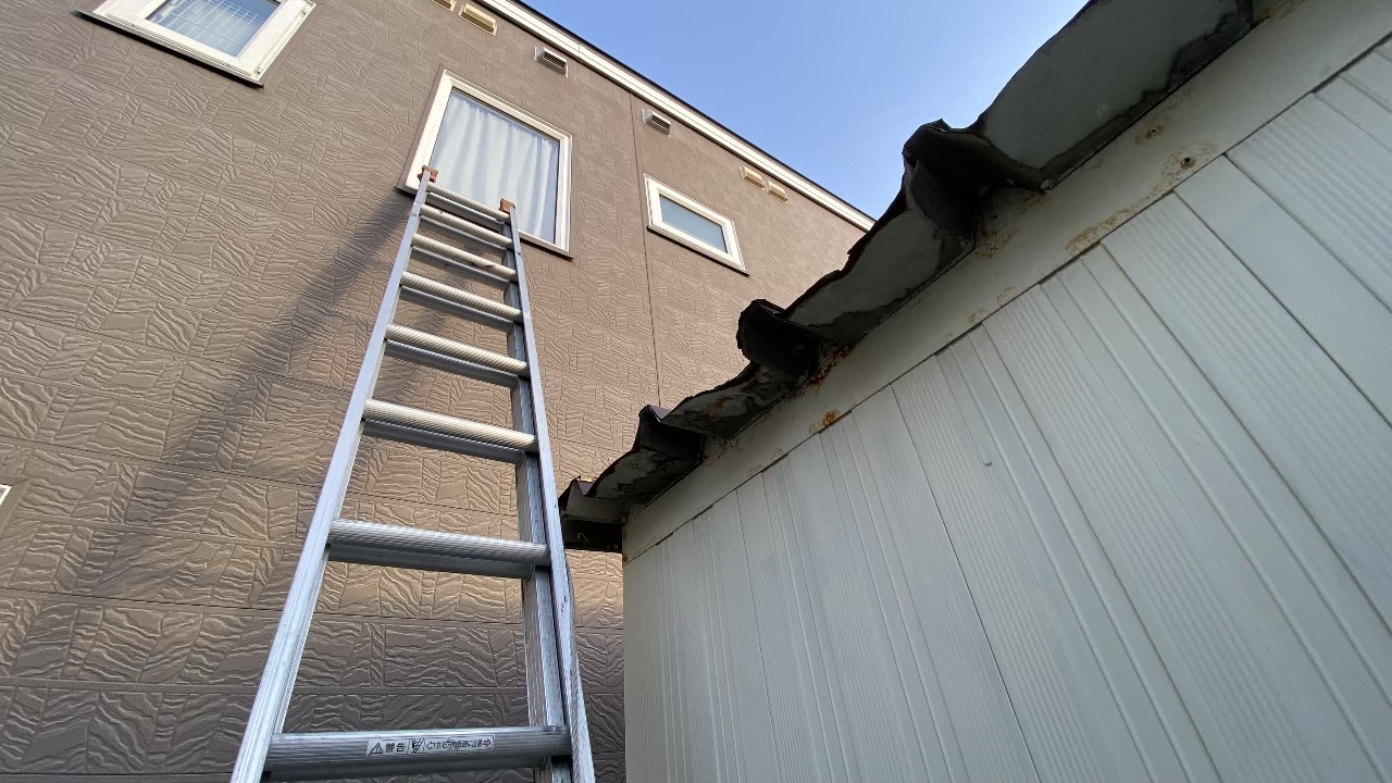 住宅の外壁に長い2段はしごを立てかけ、隣の車庫との位置関係がわかる写真