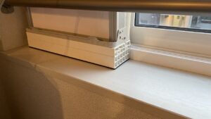 窓の木枠（額縁）の上に設置された、窓枠アタッチメントの白いプラスチック製長方形ブロックのクローズアップ写真