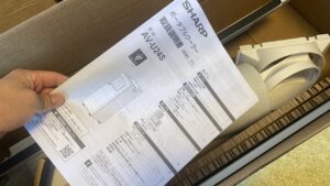 段ボール箱の上に乗せられた、シャープ製ポータブルクーラーAV-U24Sの取扱説明書の写真