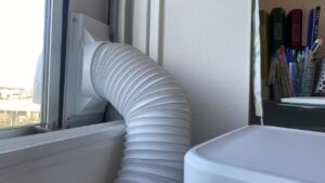 スポットクーラーの本体背後から窓のパネルへと繋がっている、太くて白い蛇腹状の排熱ダクトの写真