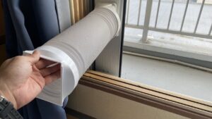 ベランダ側の大きな窓に設置されたロングパネルと、そこに固定された白い排熱ダクト（蛇腹ホース）の手元の写真
