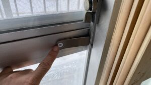 窓のサッシに取り付けられた簡易的な補助鍵のアップ写真。指で『押』と書かれたボタンに触れている