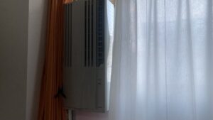 大きなテラス窓の上部に延長枠を組み合わせ、目線より高い位置にすっきりと固定されたコロナ製の窓用エアコン