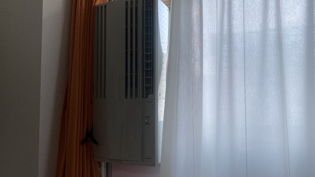 大きなテラス窓の上部に延長枠を組み合わせ、目線より高い位置にすっきりと固定されたコロナ製の窓用エアコン