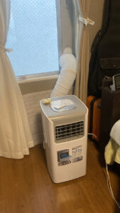 室内から引きで撮影したスポットクーラーの設置写真。加工されたパネルから太い排気ダクトが伸び、本体へと綺麗に接続されている様子
