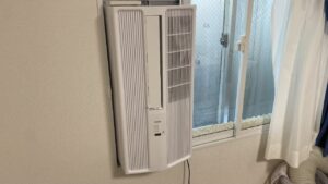窓枠に新しく設置された白いトヨトミ製の窓用エアコン。従来モデルより少し角張ったスタイリッシュなデザインになり、中央に縦長の送風口が設けられている