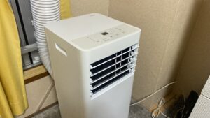 スポットクーラー本体の背面写真。下部のドレン口から透明なチューブが伸びており、床に置いたプラスチック製バケツの中に水が貯まるようにセットされている