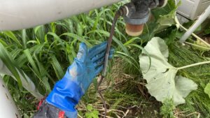 お庭の隅に設置されている大きな灯油タンクの周りの草刈り風景。タンクの下にも雑草が激しく生い茂っており、細かい配管が見えづらい状態になっている