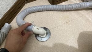 床の排水口に新しく白い排水エルボをはめ込み、そこに長さを合わせてカットした排水ホースをしっかりと接続している手元の写真
