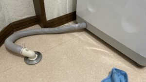 壁際に綺麗に寄せられた洗濯機の足元写真。余分な長さがなく、L字の排水エルボを通じてすっきりと床の排水口へ繋がっているホースの様子