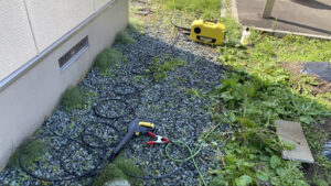 砂利敷きの地面に設置されたケルヒャーの電動高圧洗浄機本体とホース類